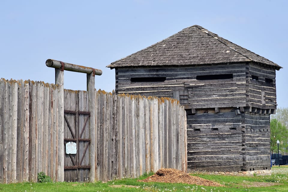 A rustic wooden structure with a thatched roof, a wooden fence, and a pile of hay.