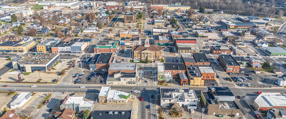 An aerial view of a town with a prominent central building, several smaller commercial buildings, and a mix of residential areas.