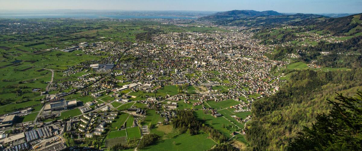 A panoramic view of a town nestled in a valley with surrounding hills and green fields.