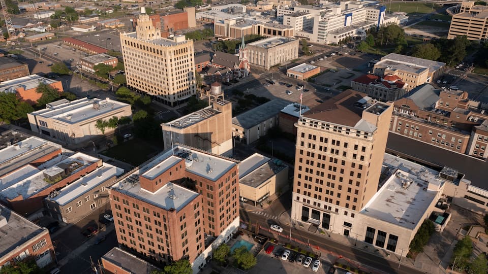 An aerial view of a cityscape with prominent buildings, including a large church with a steeple, a tall rectangular building, and several smaller structures.