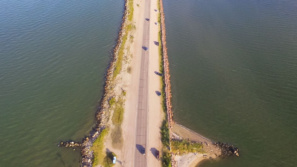 An aerial view of a coastal road with a beach on one side and a rocky shoreline on the other.