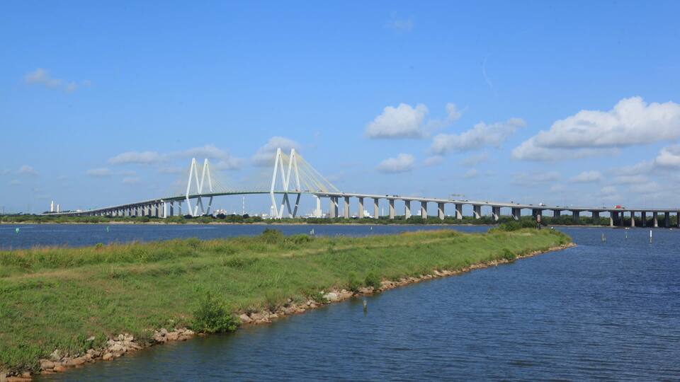 A large bridge spanning a river with grassy banks and a clear blue sky.
