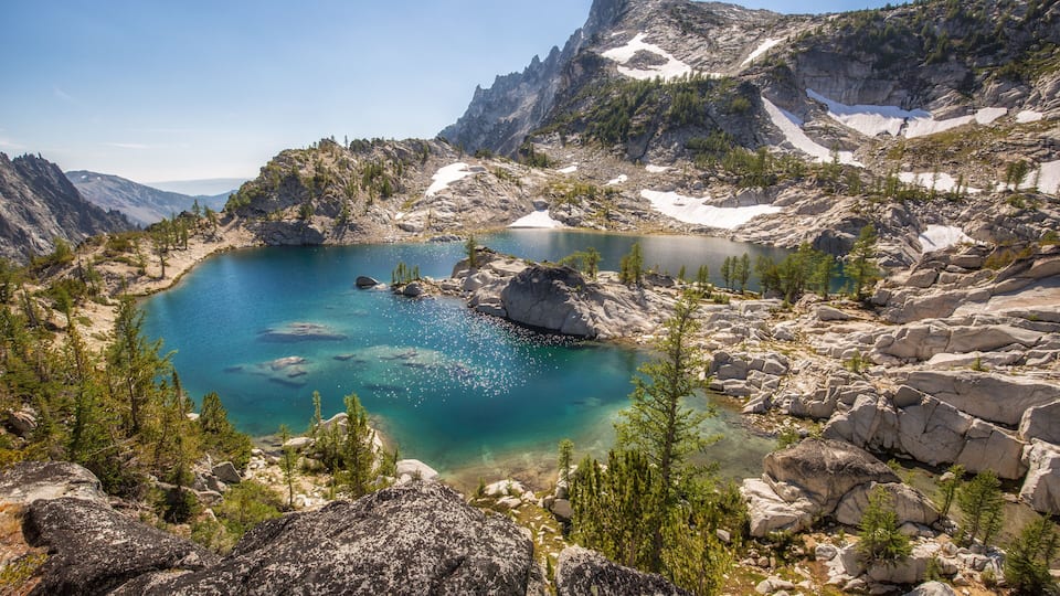 A clear mountain lake surrounded by rocky terrain and sparse vegetation.