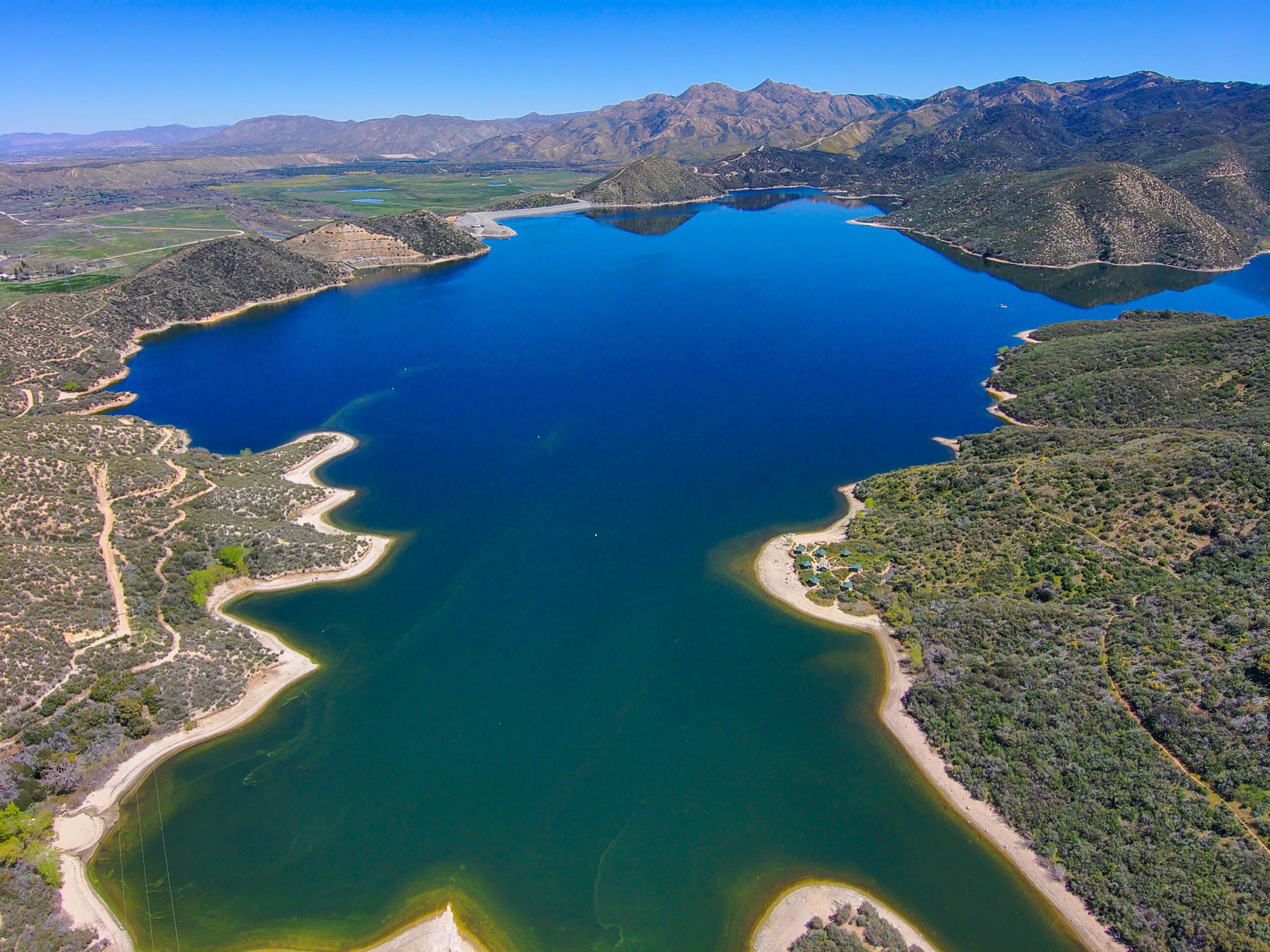 a breathtaking aerial shot of the deep still blue waters of Silverwood Lake with blue sky and lush green mountain ranges  located on the West Fork Mojave River in the San Bernardino Mountains