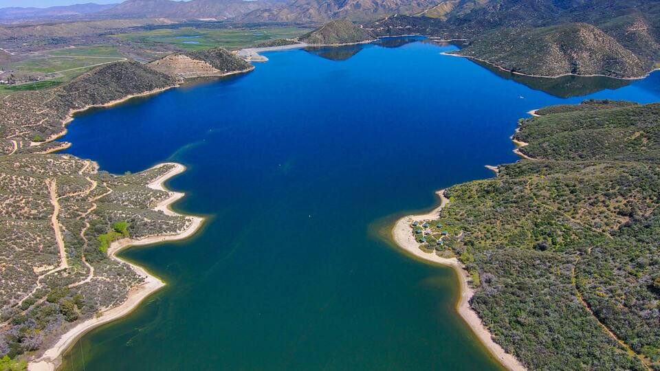 a breathtaking aerial shot of the deep still blue waters of Silverwood Lake with blue sky and lush green mountain ranges located on the West Fork Mojave River in the San Bernardino Mountains