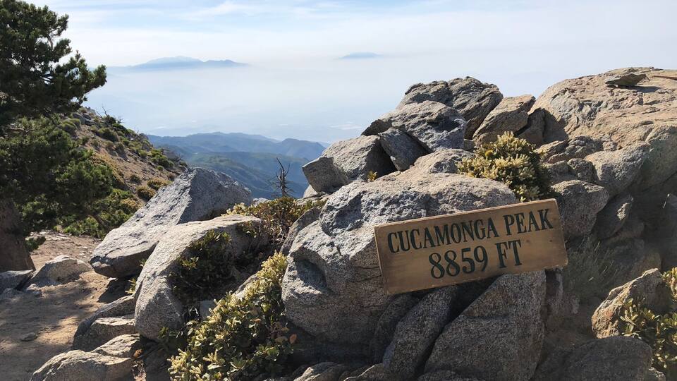 A rocky terrain with a sign indicating CUCAMONGA PEAK at 8859 FT.