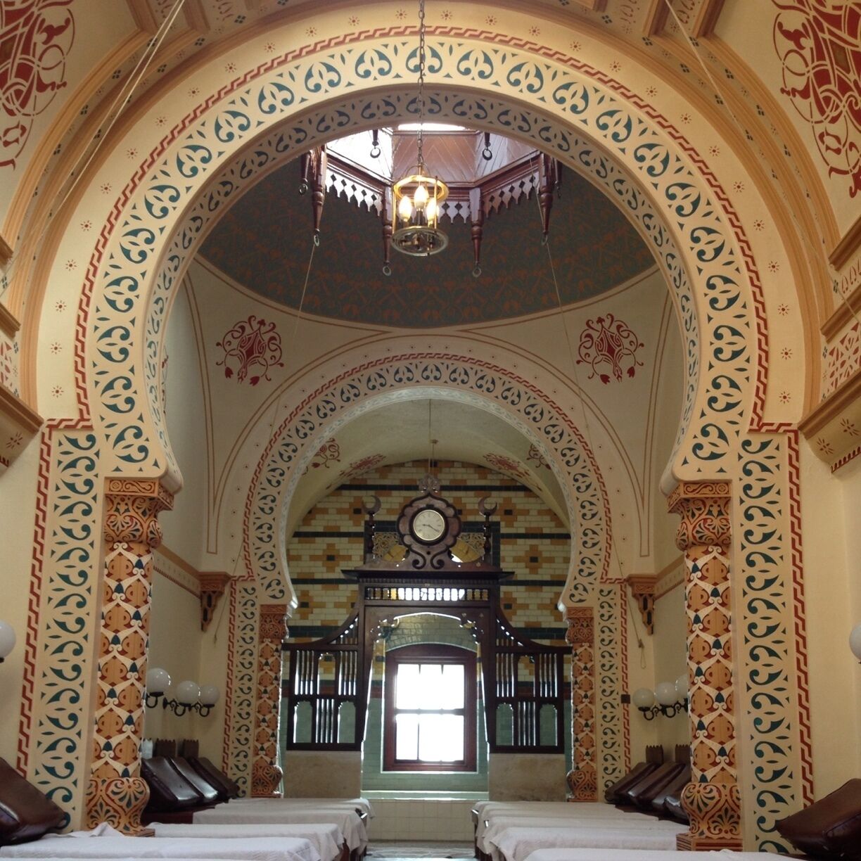 An ornate room with a large arched doorway, intricate wall patterns, and a chandelier.