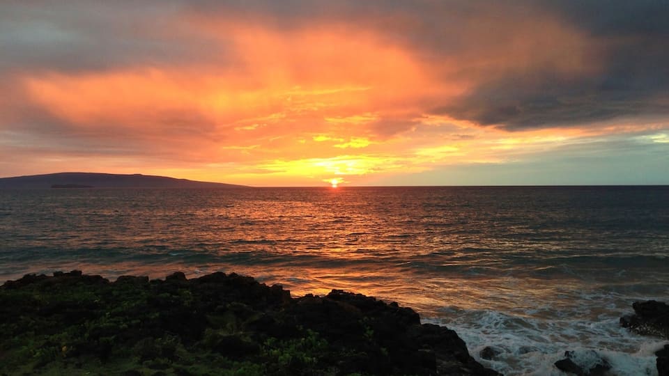 A sunset over the ocean with a rocky coastline.
