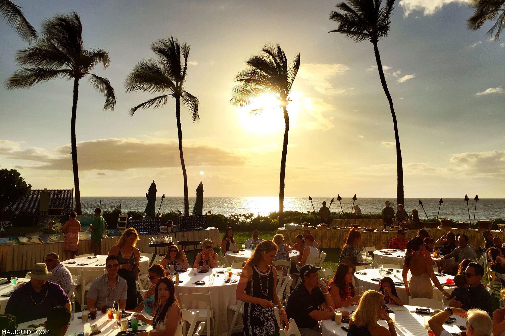 Un atardecer en un restaurante frente al mar, con palmeras y vistas al océano.