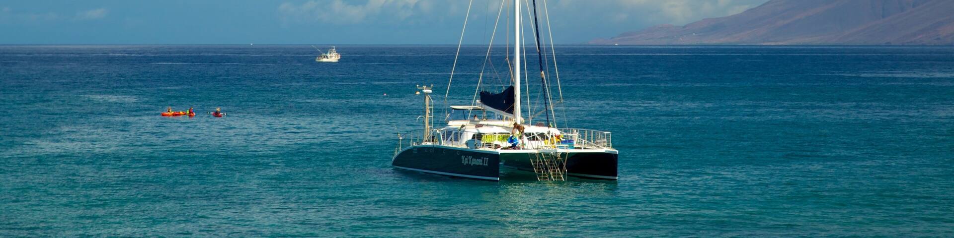 A sailboat on calm blue waters with a clear sky and distant mountains.