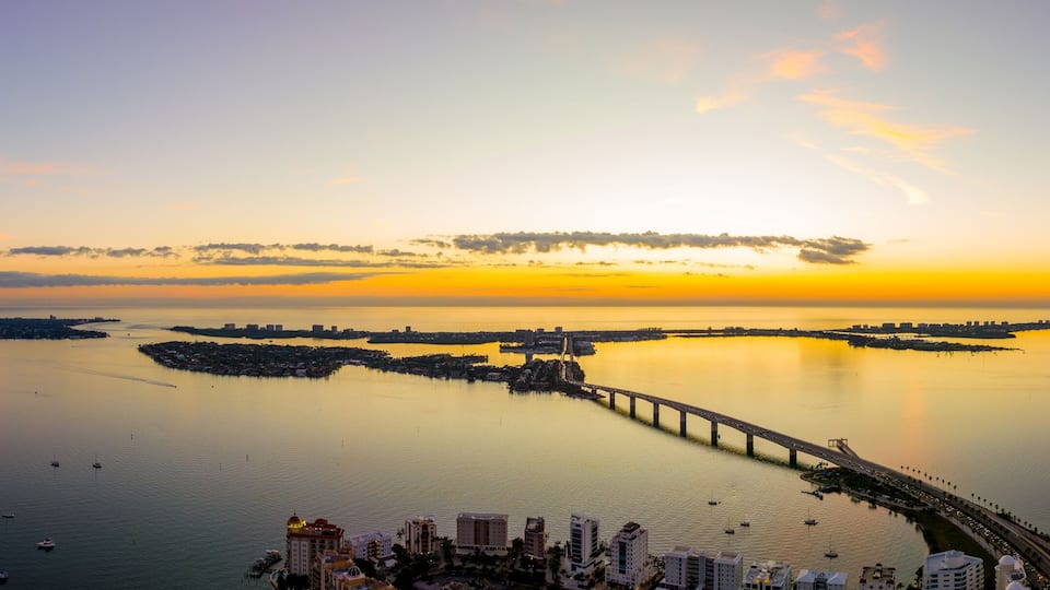 A sunset over a calm bay with a bridge and boats.