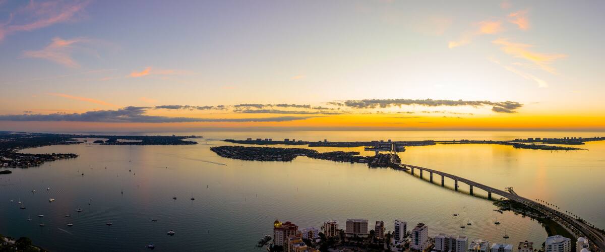 A sunset over a calm bay with a bridge and boats.
