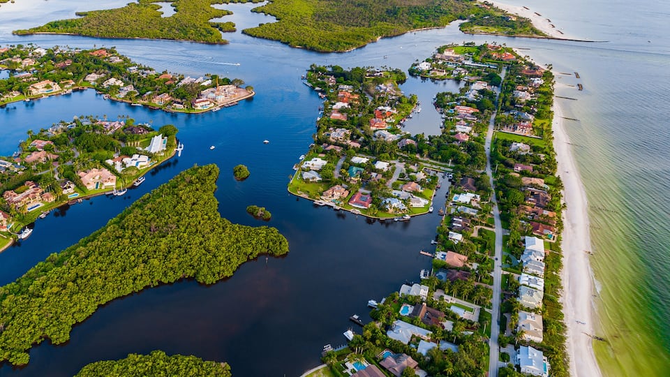 An aerial view of a coastal residential area with multiple islands connected by bridges, surrounded by water and a beach.