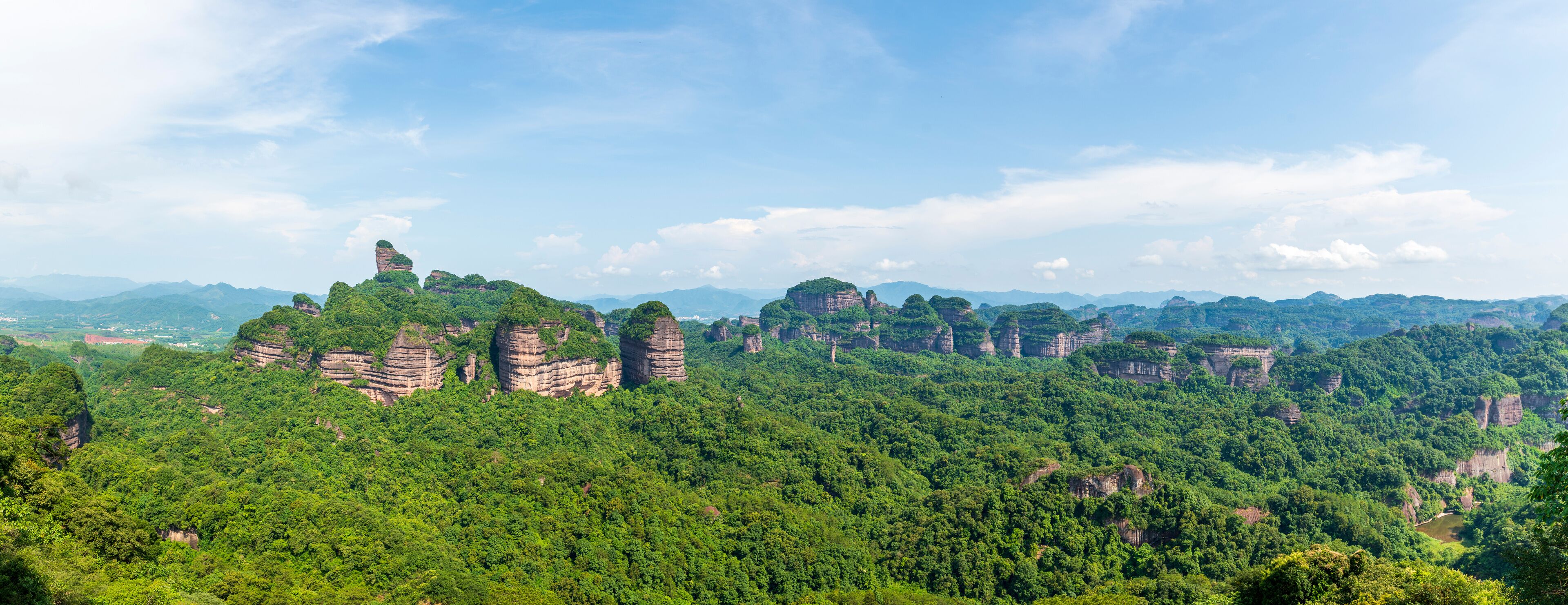 A mountainous landscape with dense green forests and prominent rock formations.