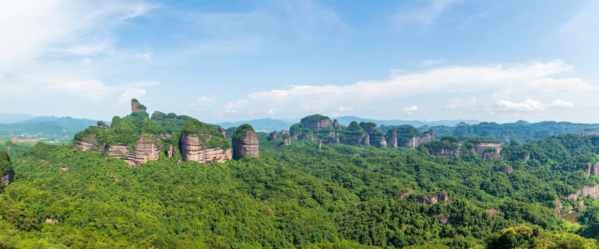 A mountainous landscape with dense green forests and prominent rock formations.