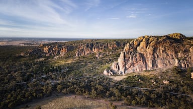 Paisagem acidentada com formações rochosas imponentes e uma área florestal densa.