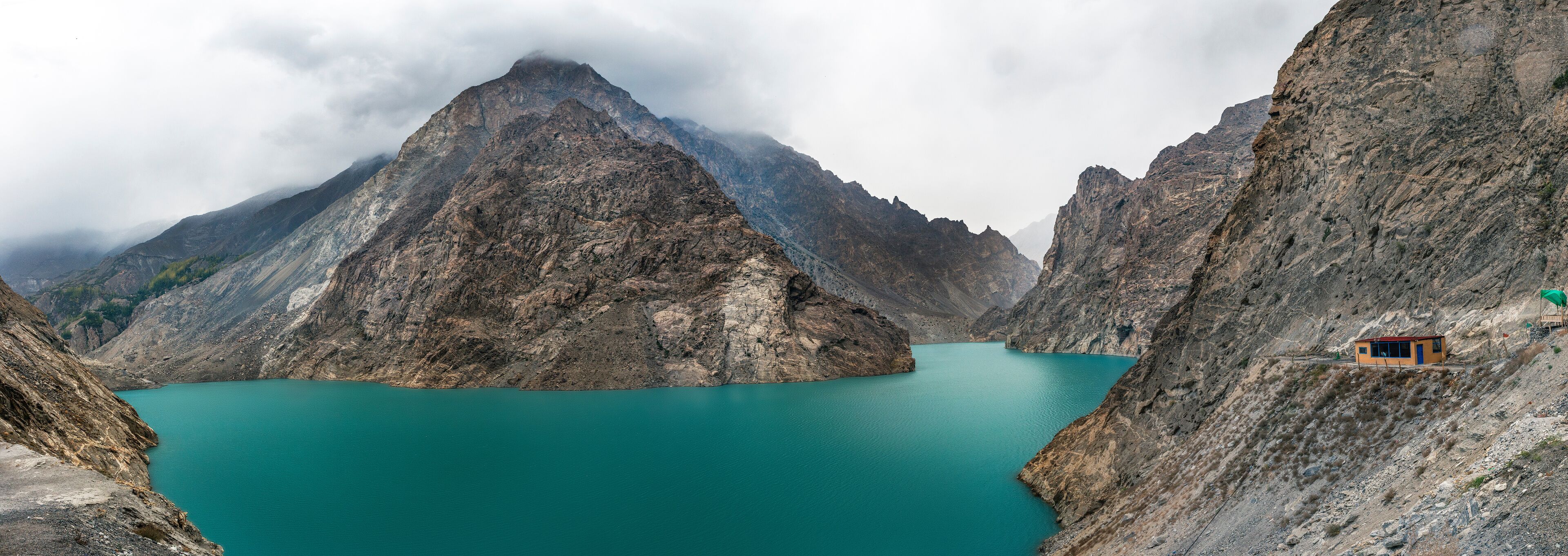 A turquoise lake surrounded by rugged mountains, with a small cabin on the right.
