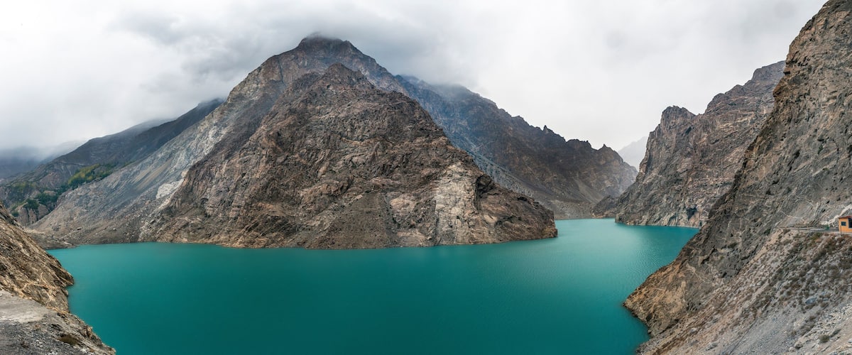 A turquoise lake surrounded by rugged mountains, with a small cabin on the right.