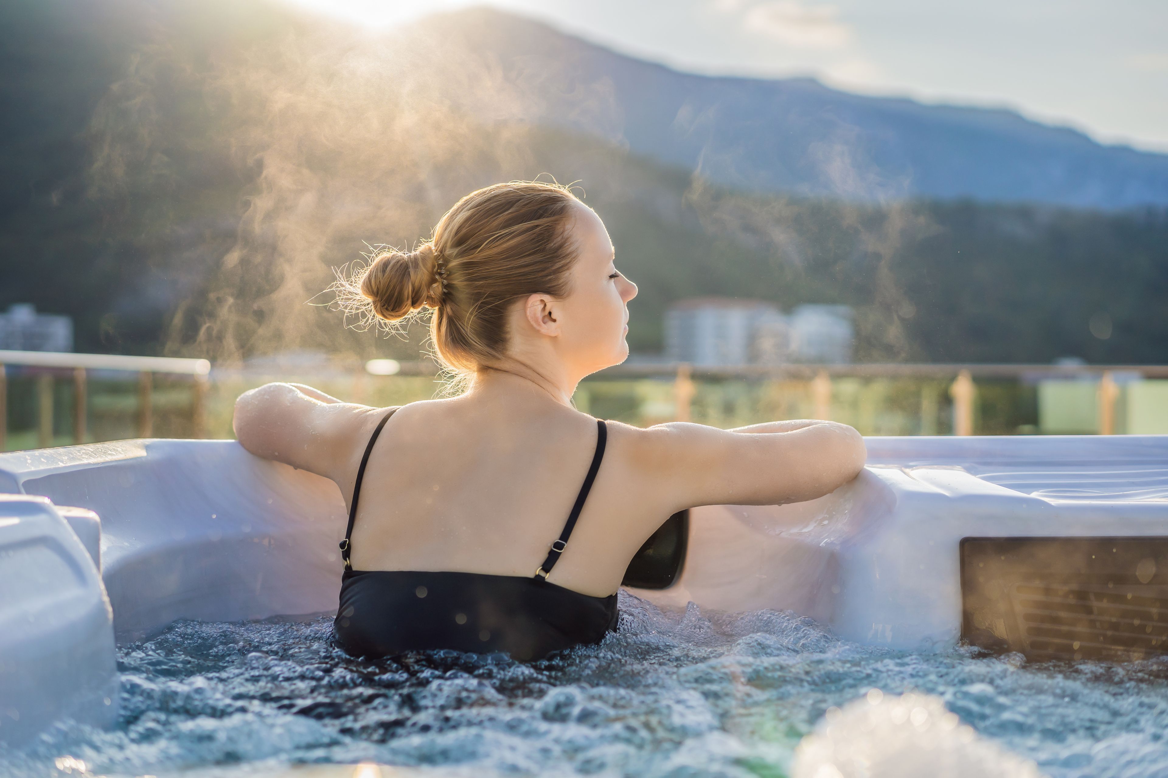 A person in a hot tub with a mountainous landscape in the background.