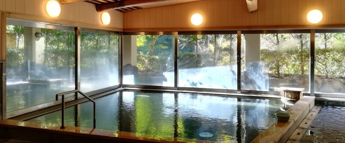A large indoor swimming pool with glass walls, wooden ceiling beams, and a stone-tiled floor.