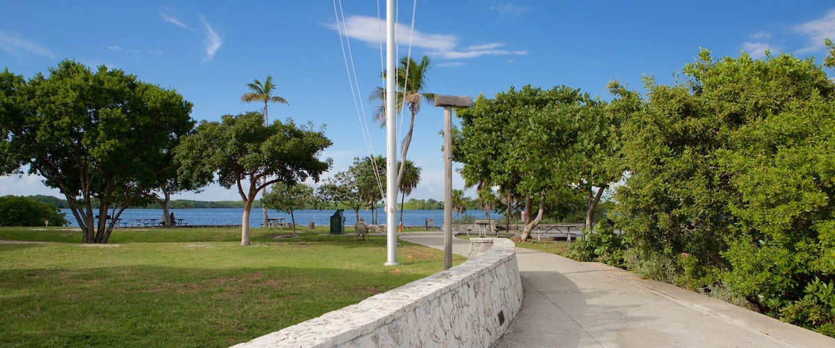 A park with a flagpole, trees, a pathway, and a body of water in the background.