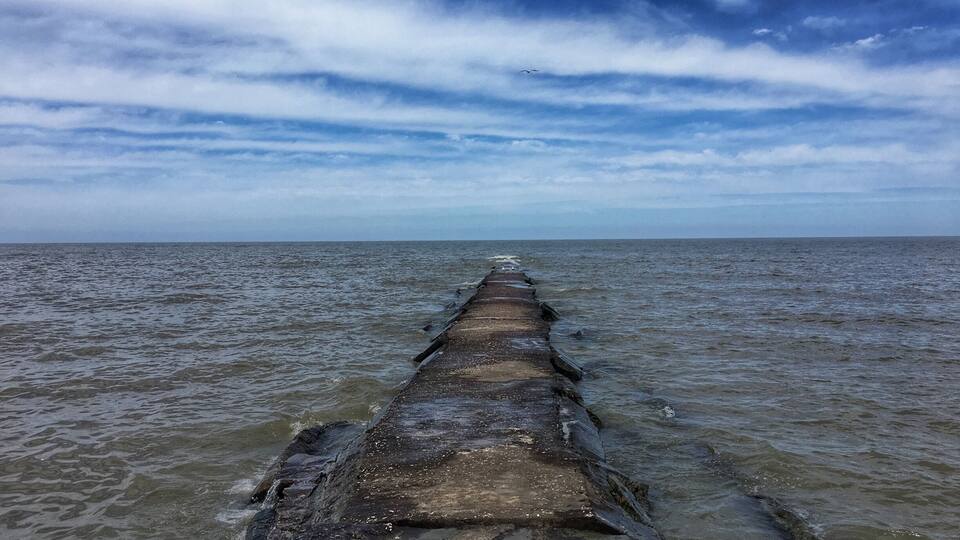 A long pier extending into the ocean under a cloudy sky.