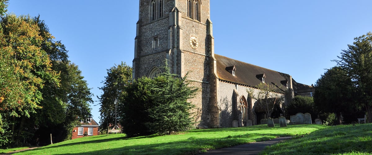 A historic church with a tall tower, surrounded by lush greenery and a clear blue sky.