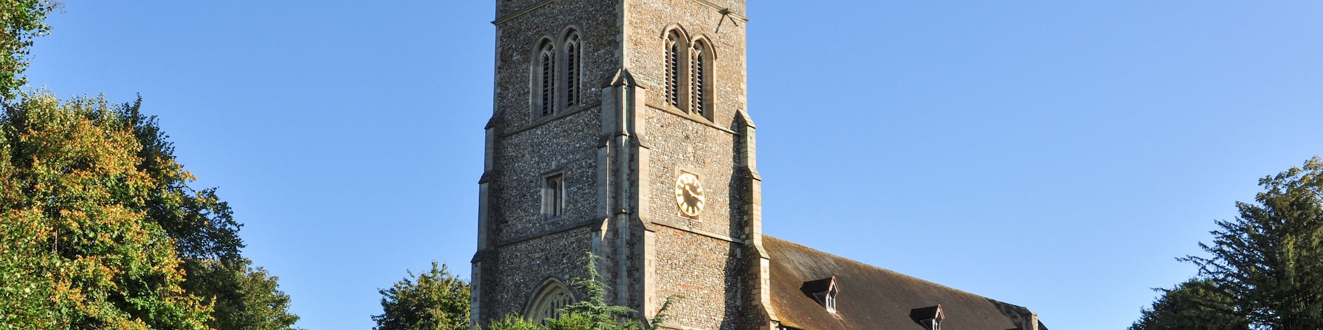 A historic church with a tall tower, surrounded by lush greenery and a clear blue sky.