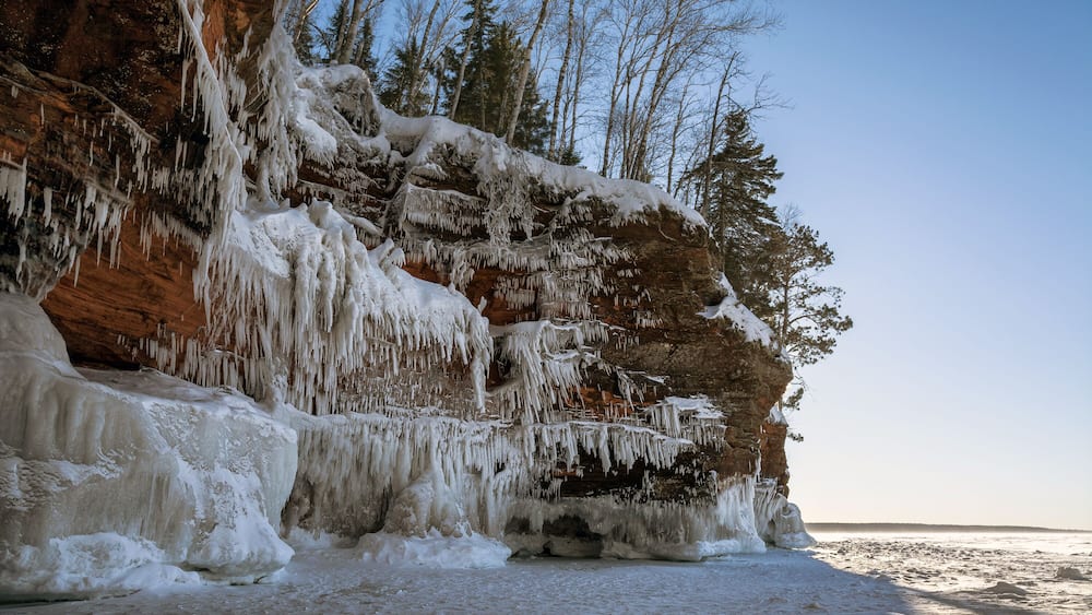 Um penhasco congelado com iciclos e árvores cobertas de neve.