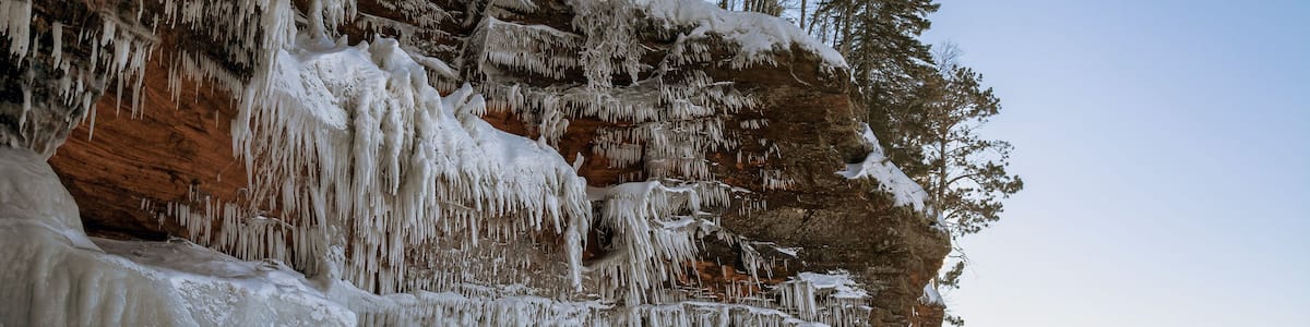 Une falaise gelée, parée de stalactites et d’arbres recouverts de neige.