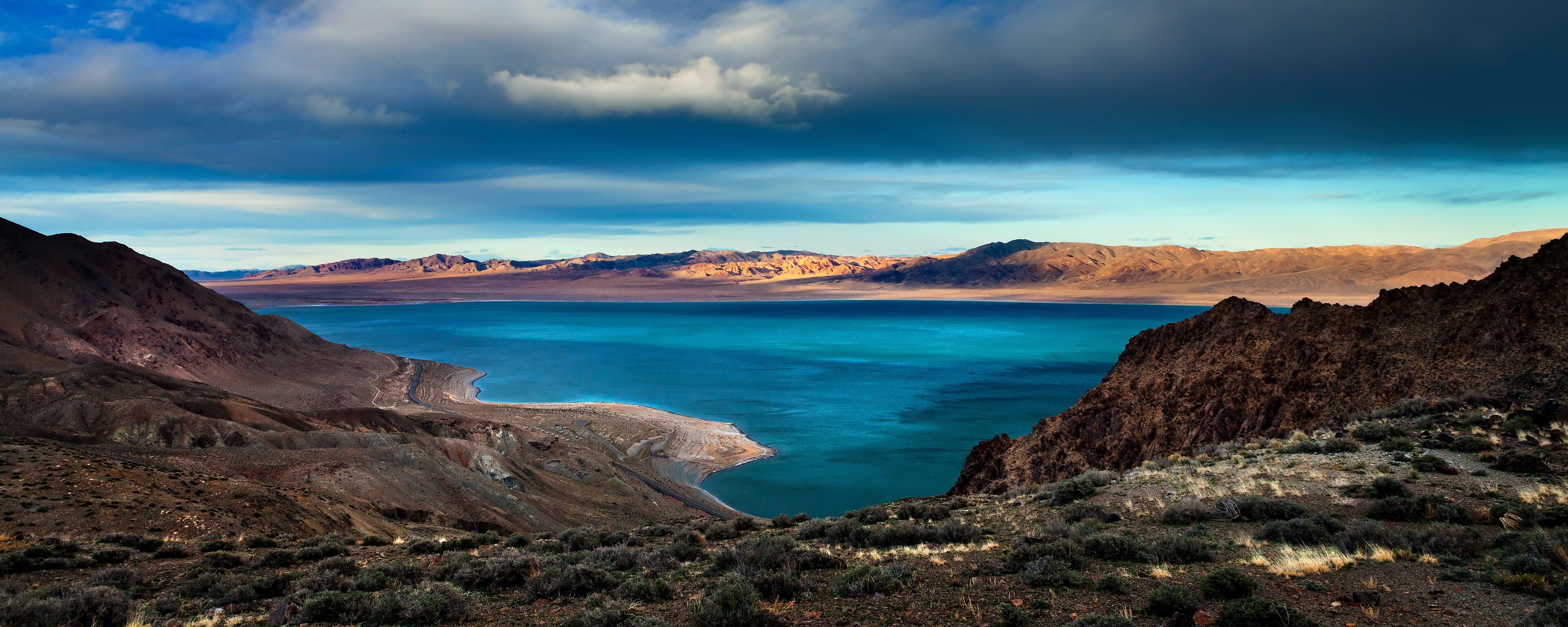 A coastal landscape with mountains, a clear blue lake, and a winding road.