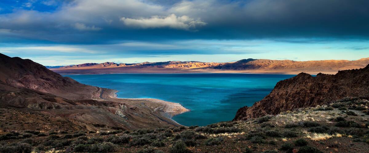 A coastal landscape with mountains, a clear blue lake, and a winding road.