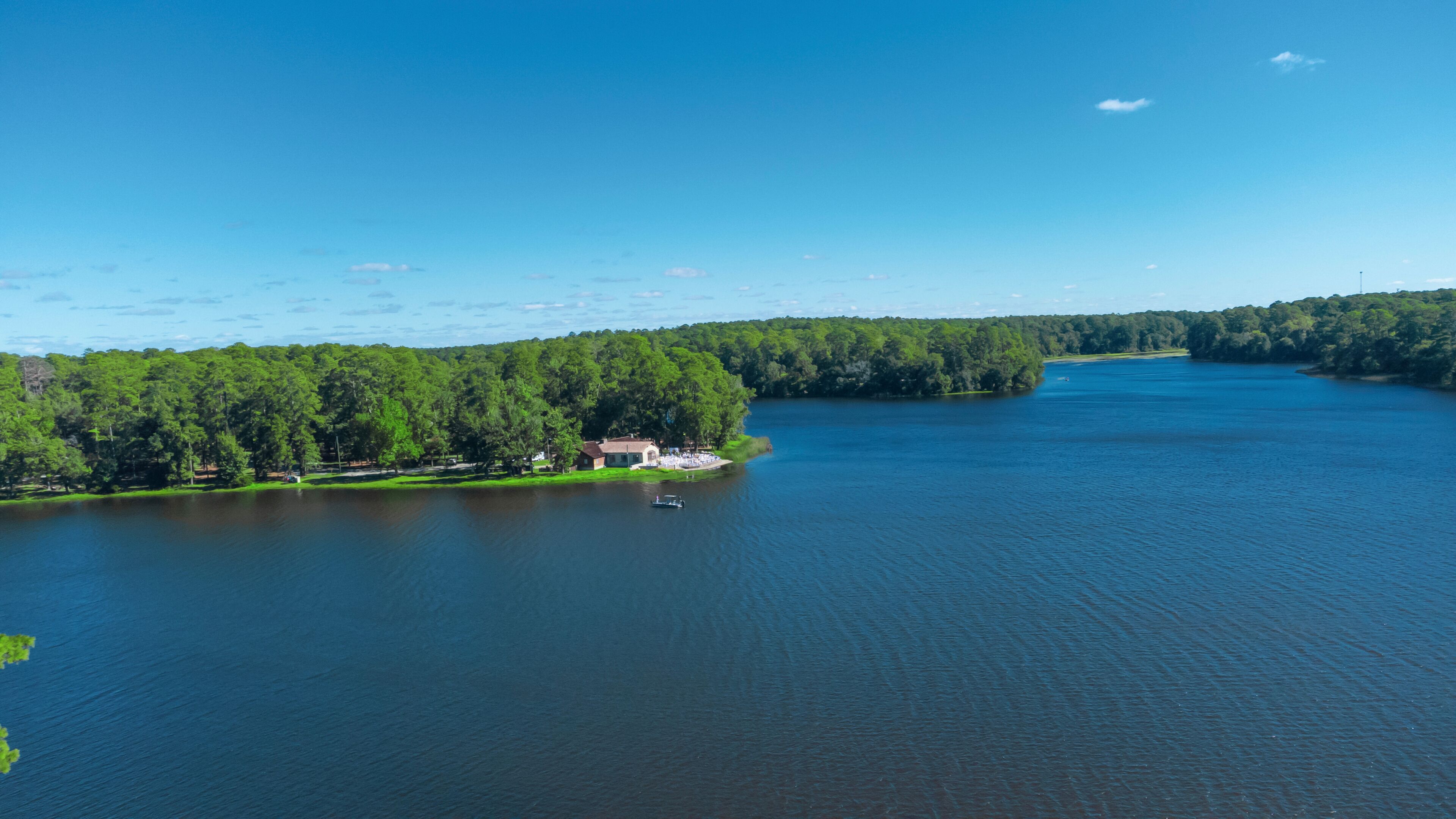 A lake surrounded by dense forest, a small house by the water's edge, and a boat on the lake.