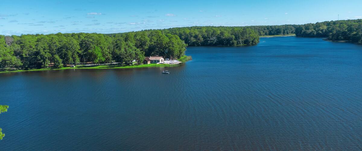 A lake surrounded by dense forest, a small house by the water's edge, and a boat on the lake.