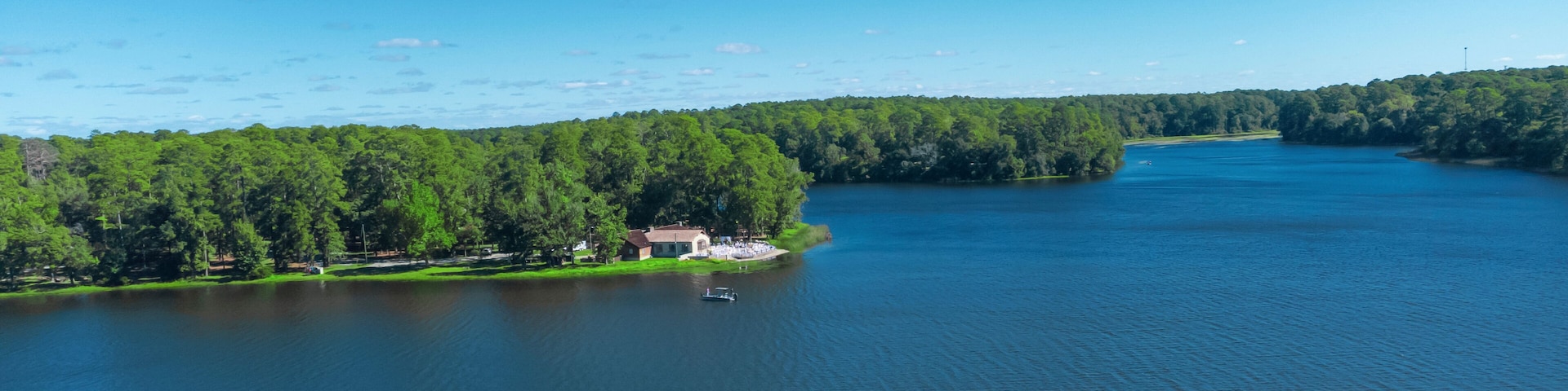 A lake surrounded by dense forest, a small house by the water's edge, and a boat on the lake.