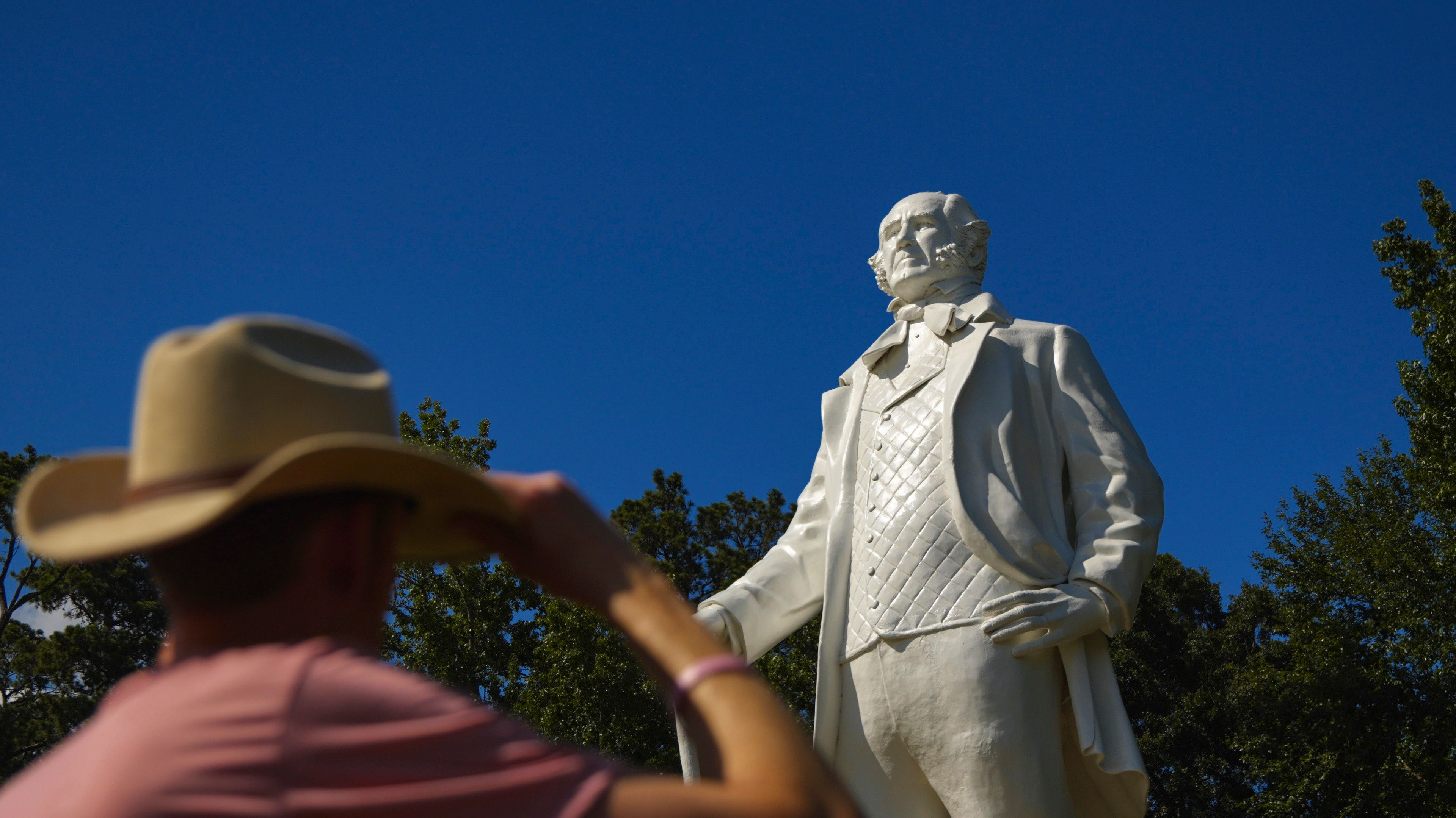 A person wearing a cowboy hat and pink shirt standing in front of a statue.