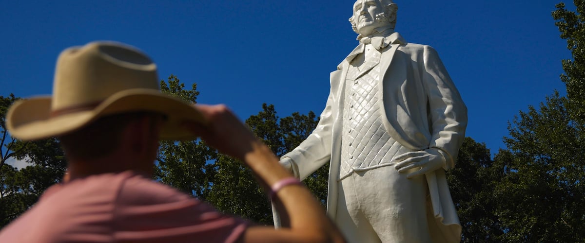 A person wearing a cowboy hat and pink shirt standing in front of a statue.