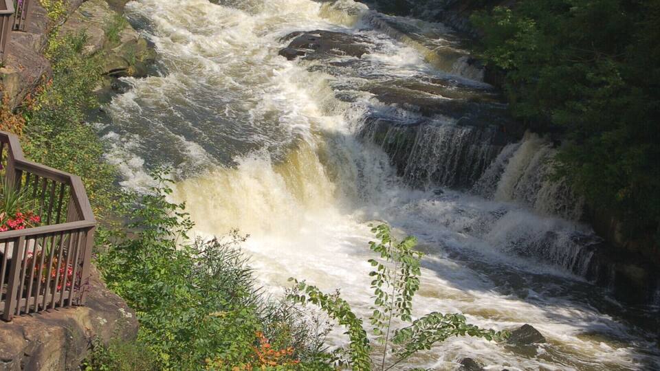 A waterfall cascading down a rocky riverbed, surrounded by lush greenery and a viewing platform.