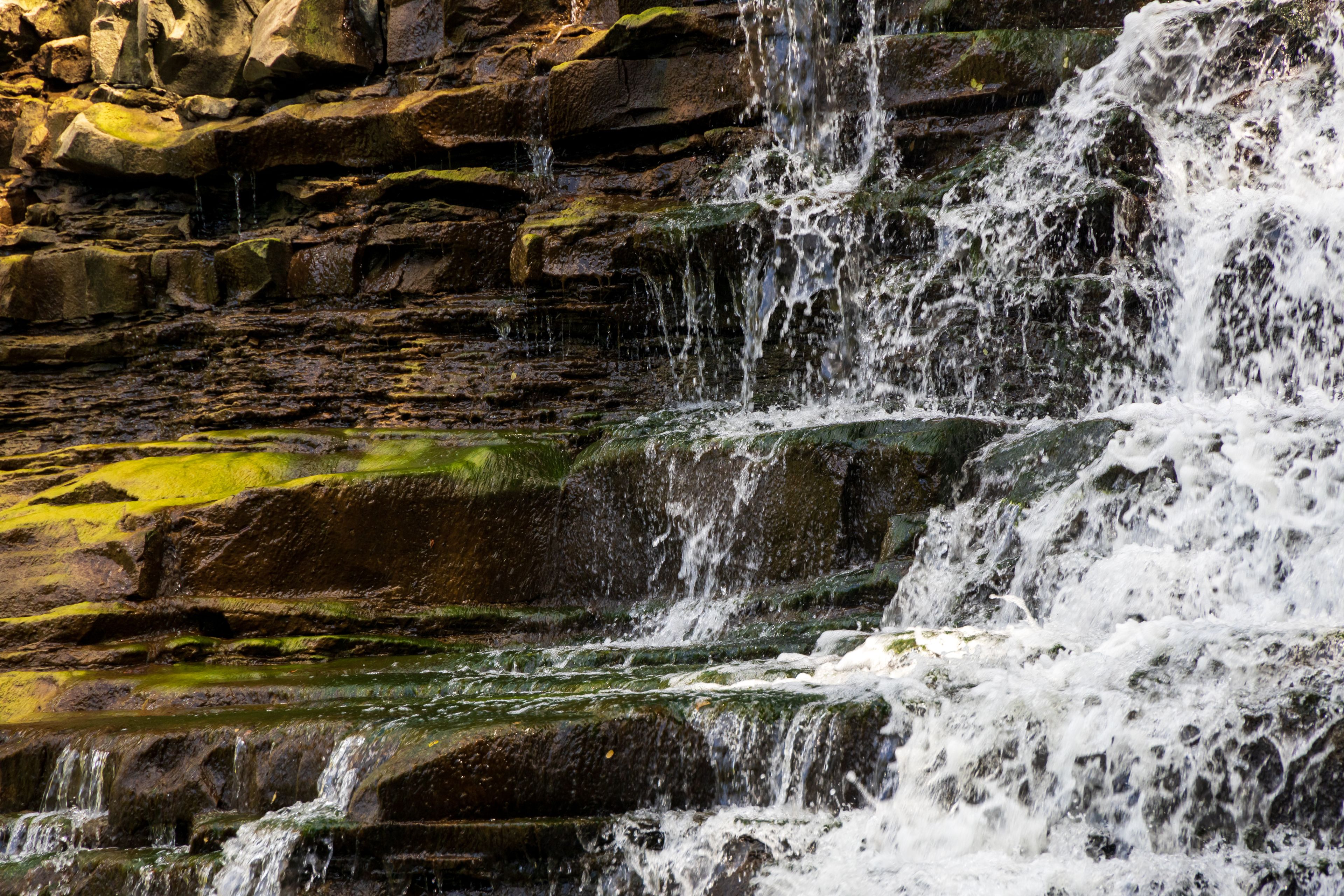 Une cascade d’eau qui dévale sur un terrain rocheux, les pierres étant recouvertes de mousse.