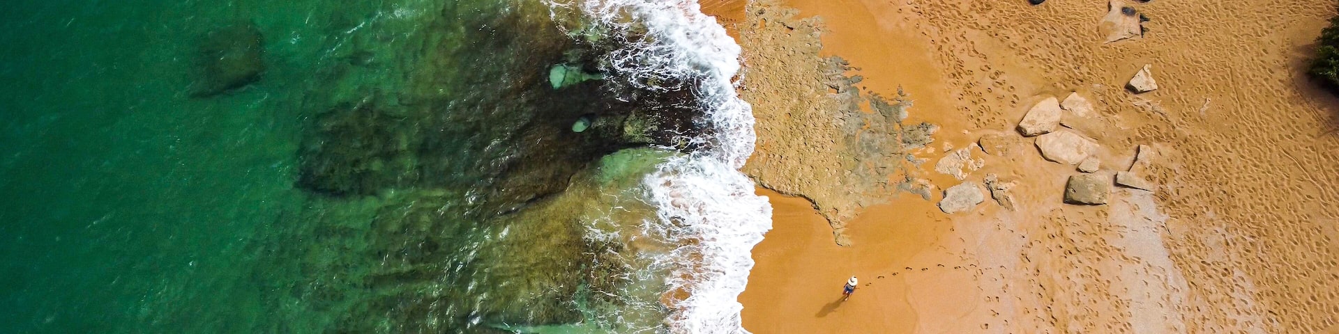Lone person walking on Red sand beach on tropical island from above