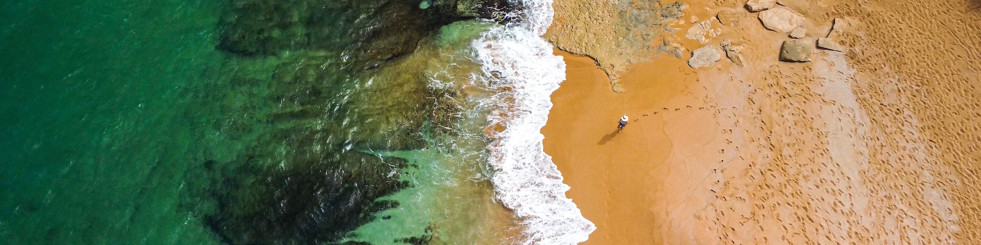 Lone person walking on Red sand beach on tropical island from above