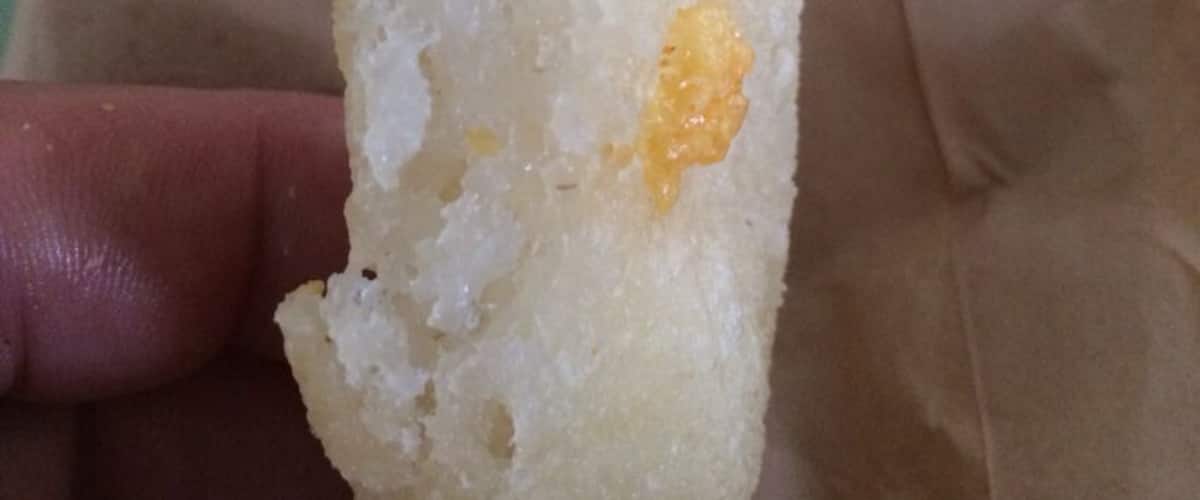 A hand holding a piece of bread with a bite taken out of it.