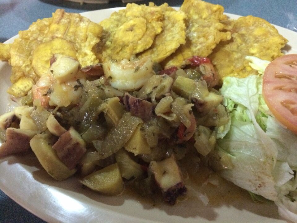 A plate with fried plantains, a mixed vegetable dish, lettuce, and a slice of tomato.