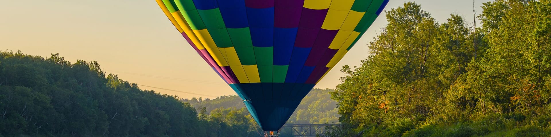 A hot air balloon over a calm river with a forested riverbank.
