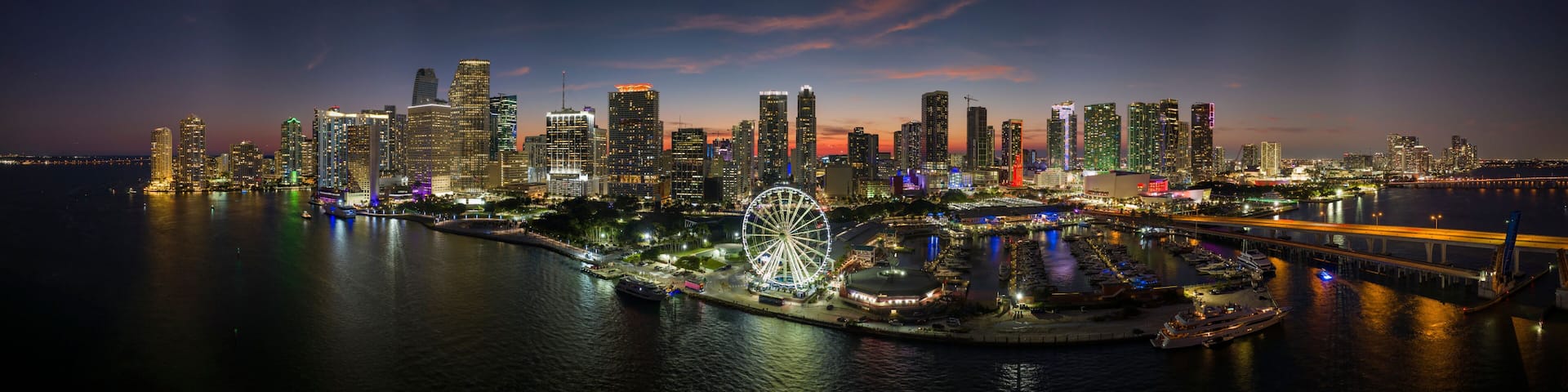 American urban landscape at night. Miami marina and Skyviews Observation Wheel at Bayside Marketplace with reflections in Biscayne Bay water and skyscrapers of Brickell, city's financial center