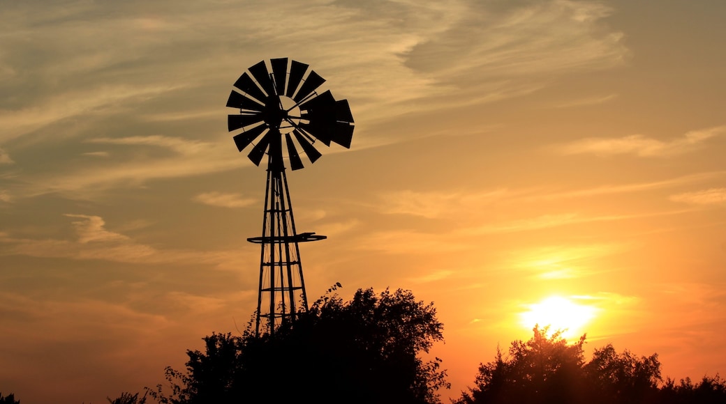 windmill at sunset with tree's,clouds, and the Sun north of Hutchinson Kansas USA out in the country.