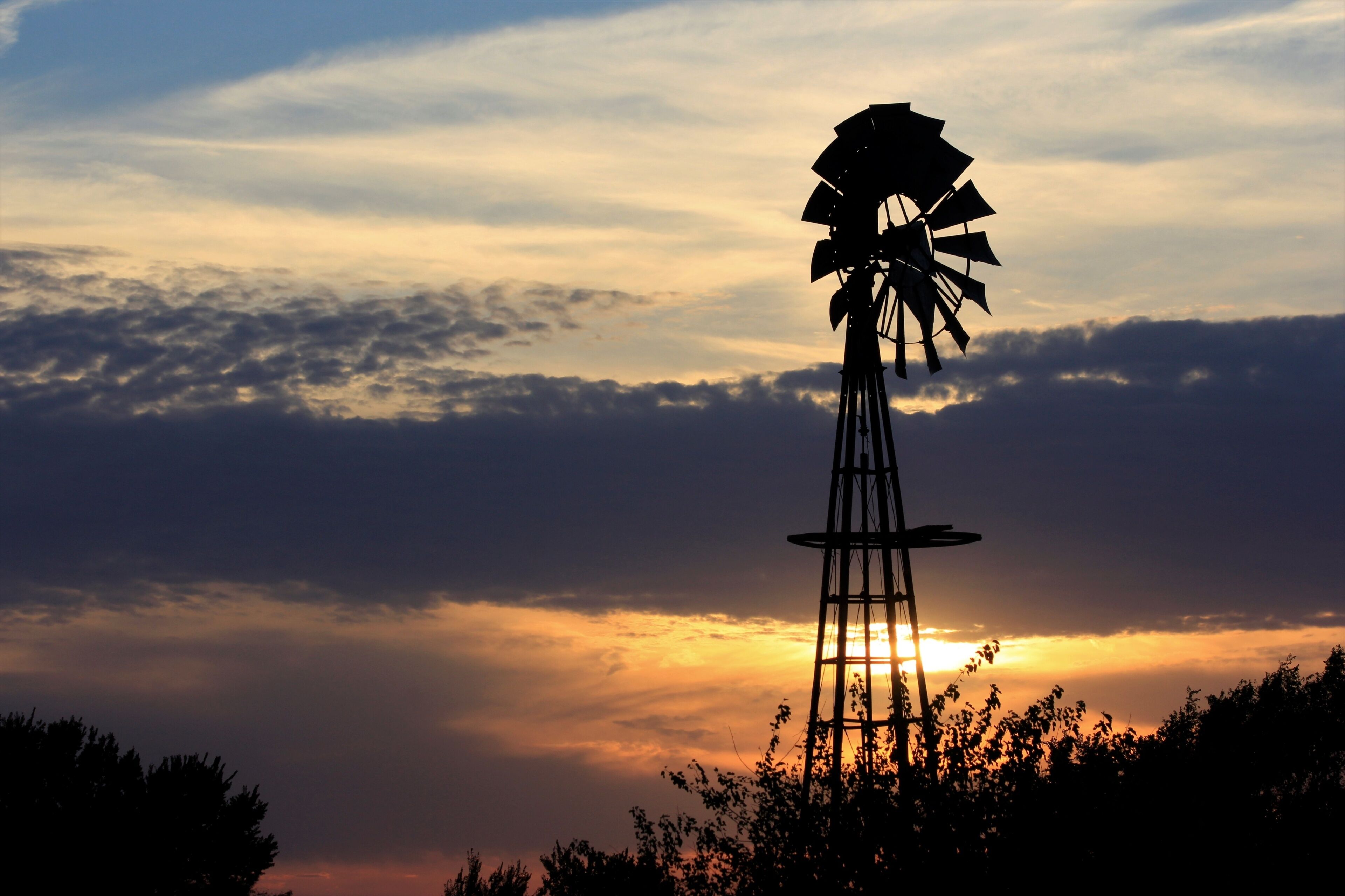 Kansas Sunset with a colorful sky and clouds with a Windmill silhouette north of Hutchinson Kansas USA.