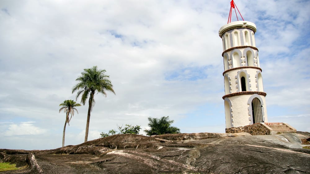 A white tower with a red antenna, palm trees, and rocky terrain.