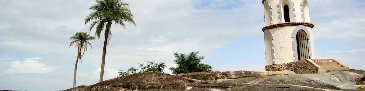 A white tower with a red antenna, palm trees, and rocky terrain.