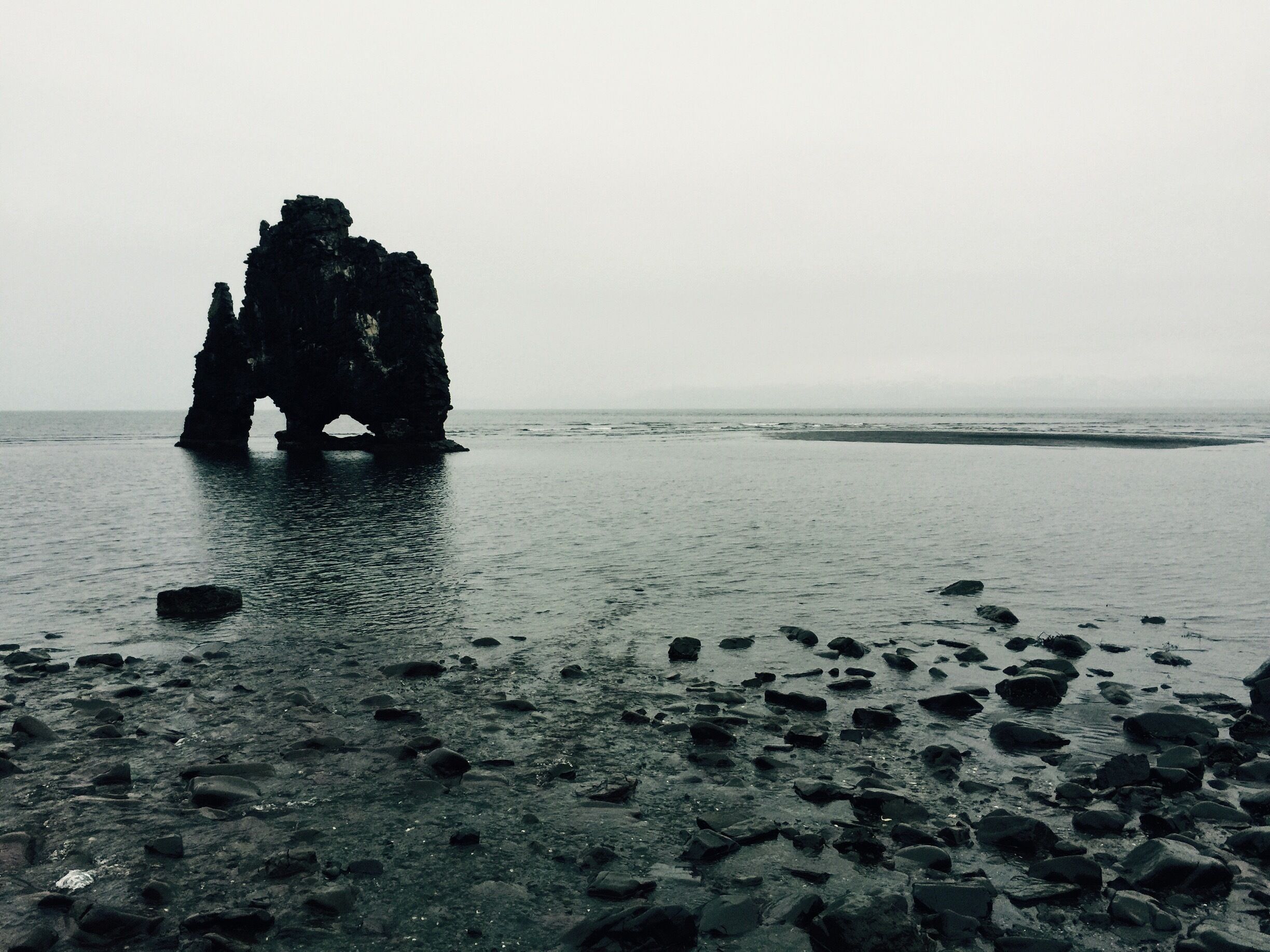 A rocky shoreline with a prominent rock formation in the water.